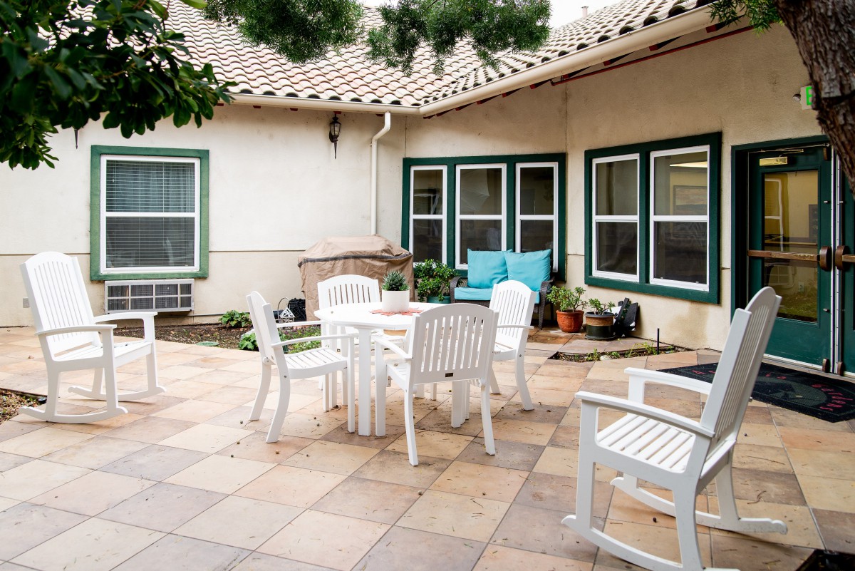 A cozy patio with white outdoor furniture and plants against a home's exterior.