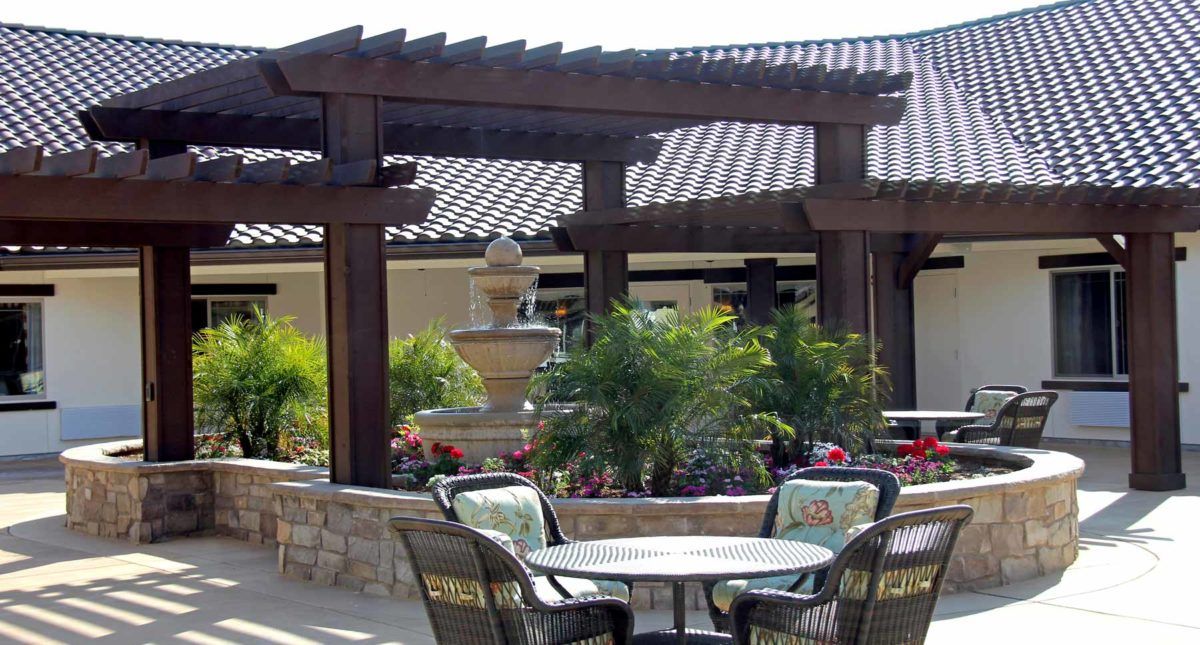 A beautifully landscaped patio area with a pergola, seating, a fountain, and lush greenery.