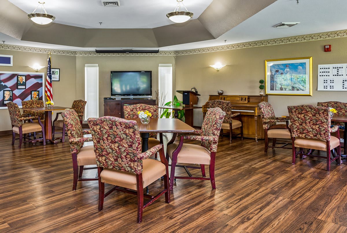 A cozy living room with wooden flooring, featuring several chairs and tables, a television, and a piano.