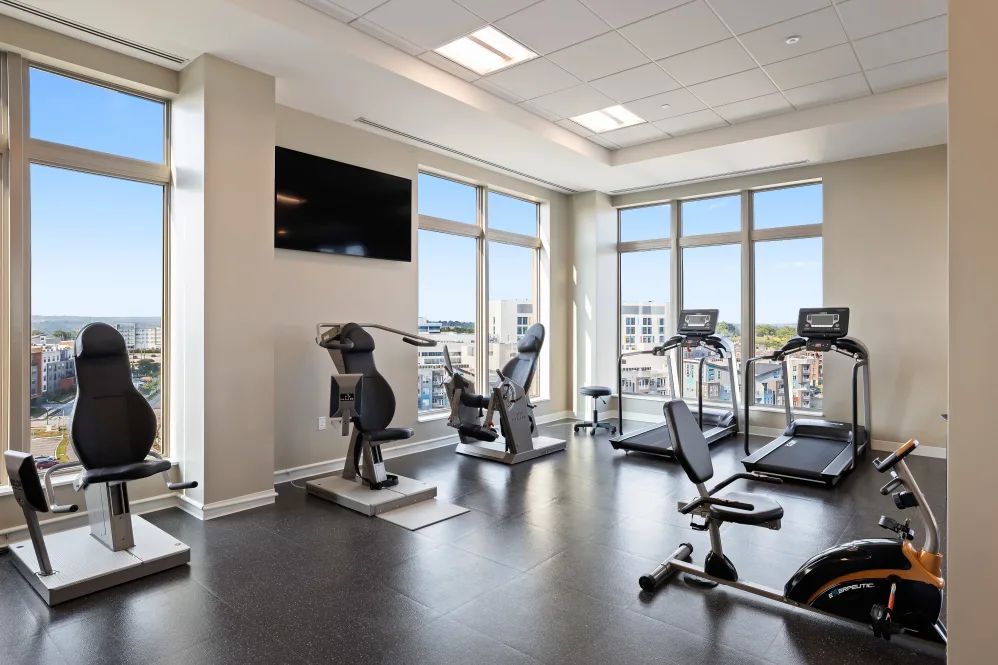 A modern gym with large windows, featuring exercise equipment like treadmills and bikes.
