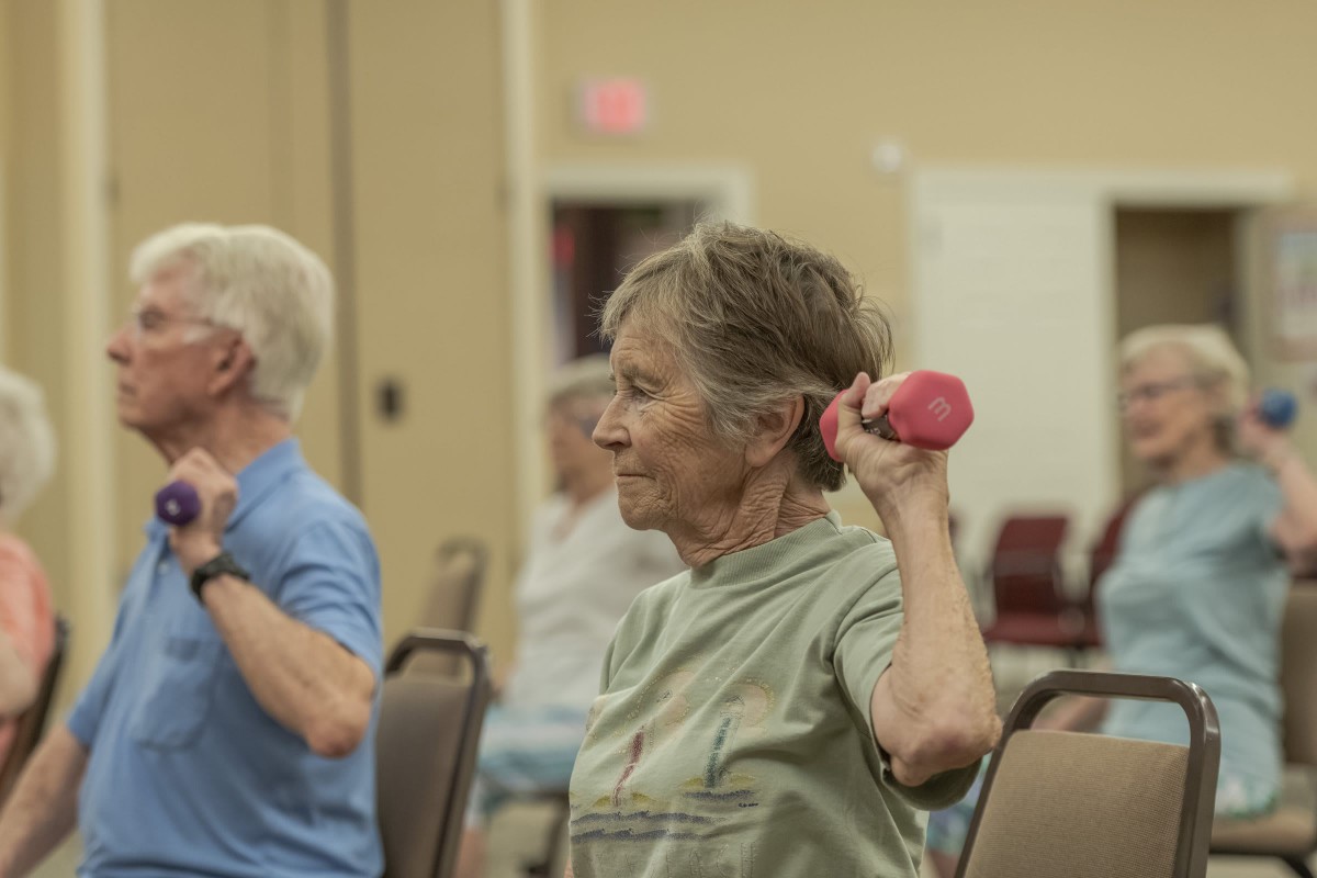 A group of seniors participating in a fitness class, lifting small weights indoors.