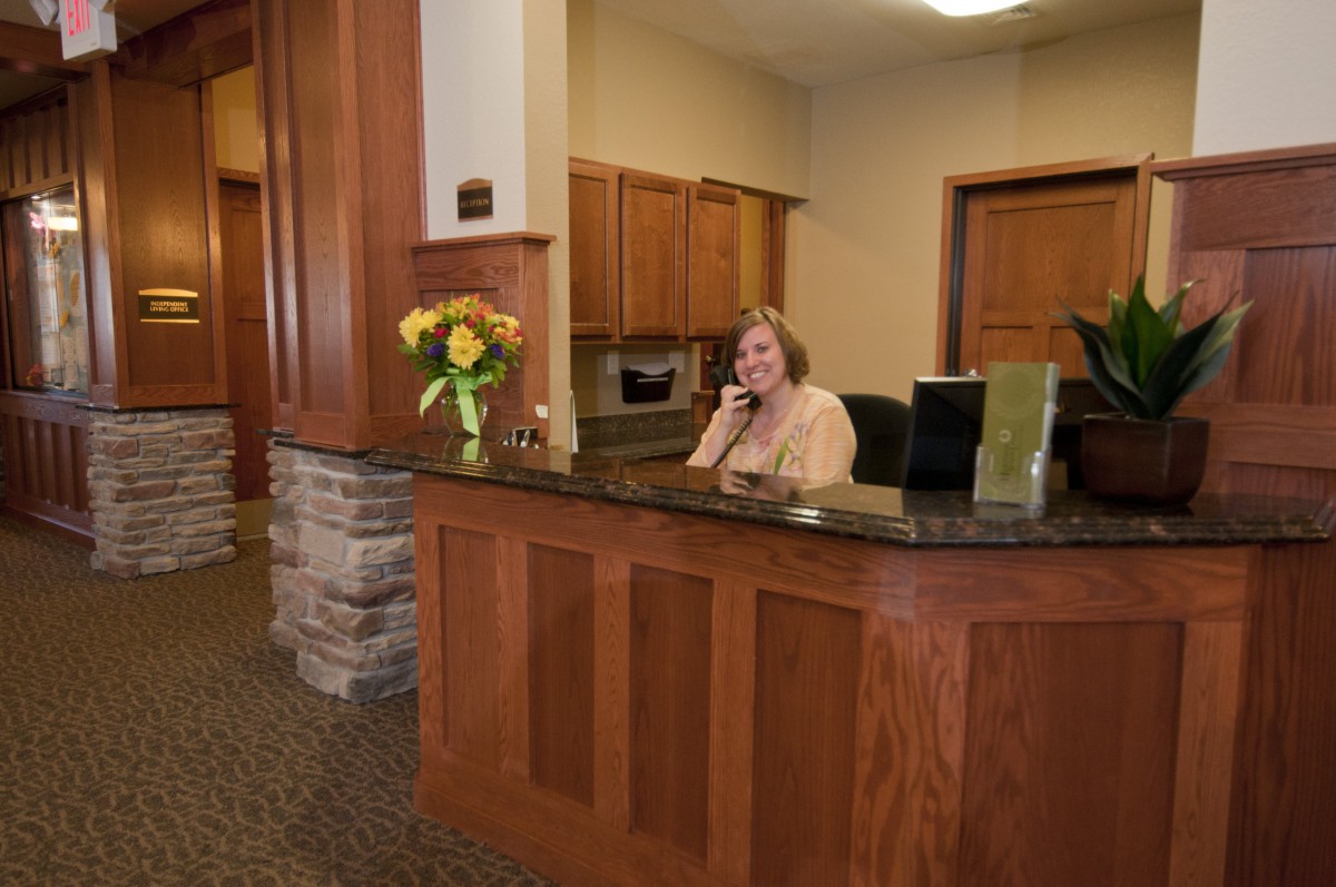 A woman speaking on the phone at a reception desk in an office setting.