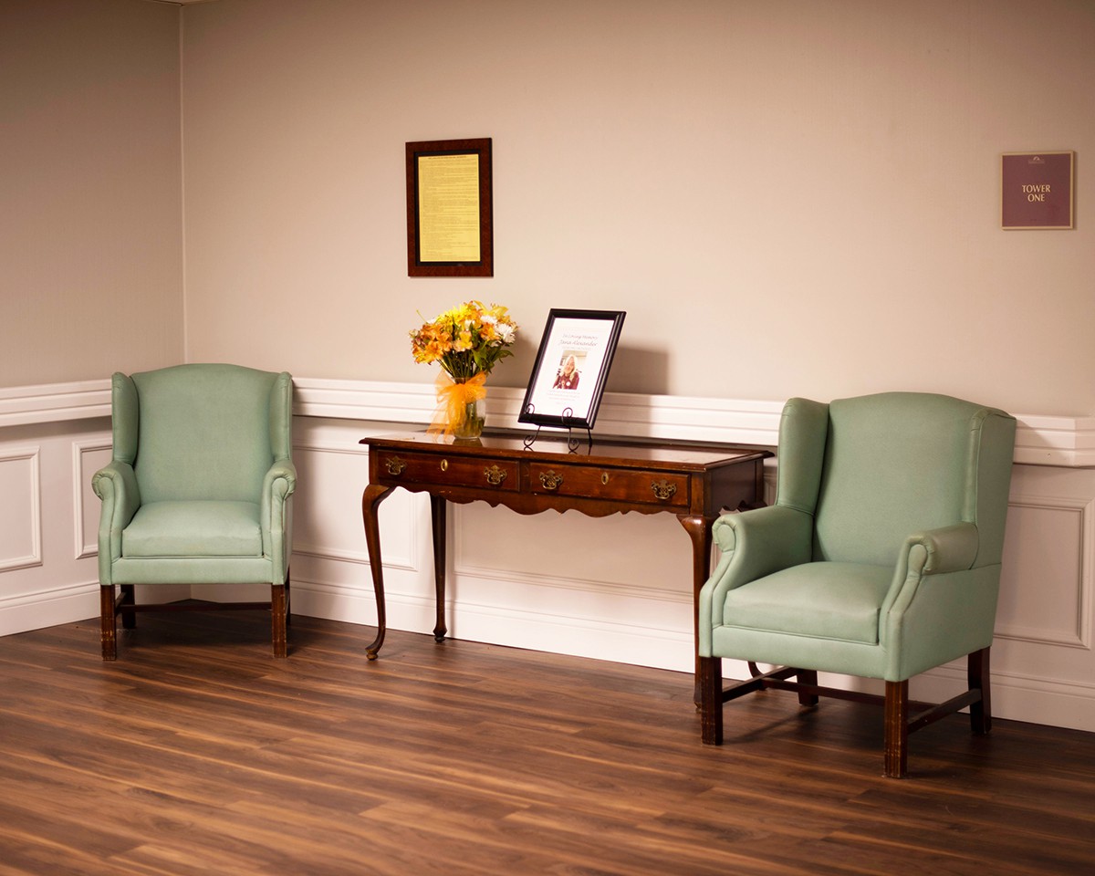 A cozy living room setting with two green armchairs, a wooden console table, and decorative items including flowers and framed pictures.