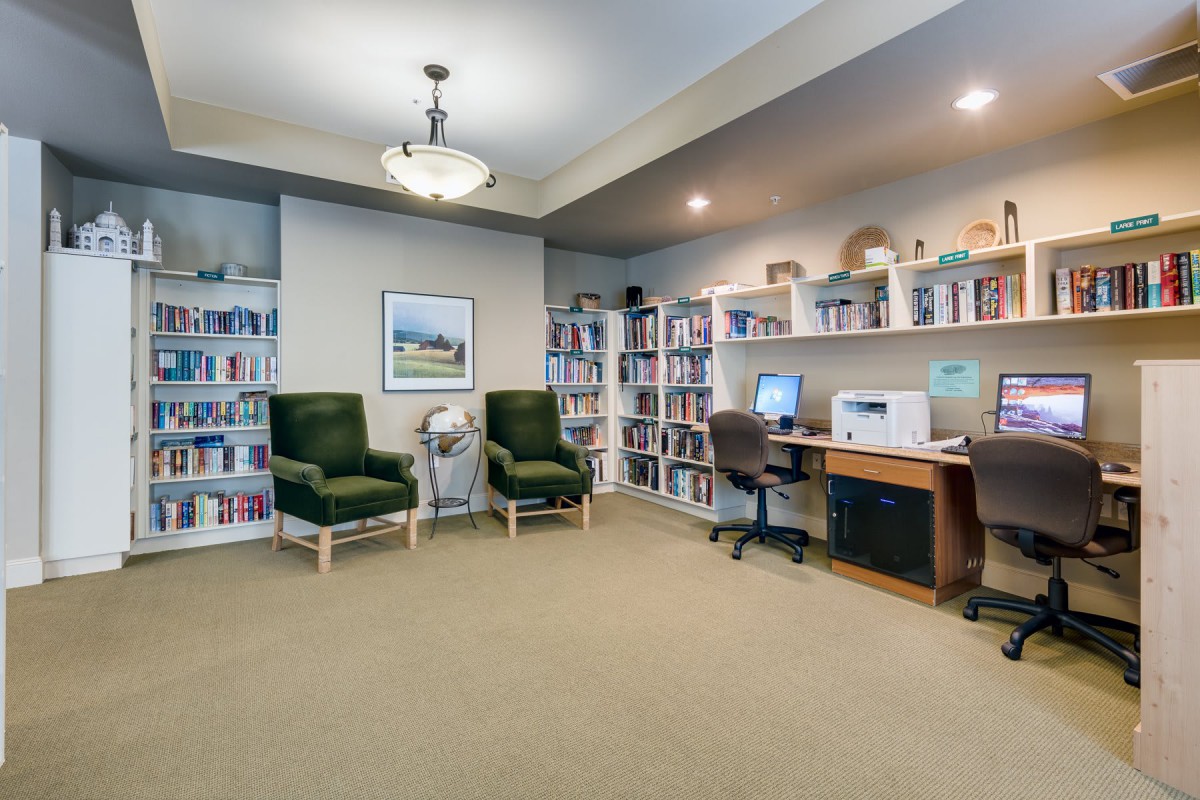 A cozy library reading area with bookshelves, comfortable chairs, and a computer desk.