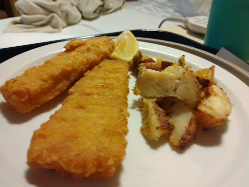 A delicious plate of fried fish fillets served with golden roasted potatoes and a slice of lemon.