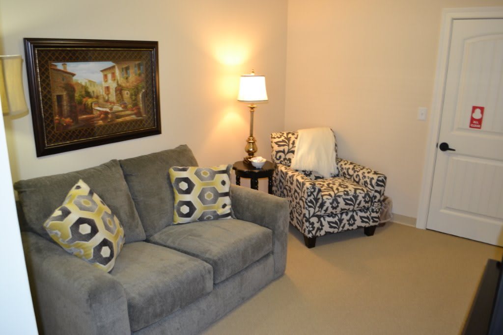 A cozy living room with a gray couch, patterned armchair, and soft lighting.