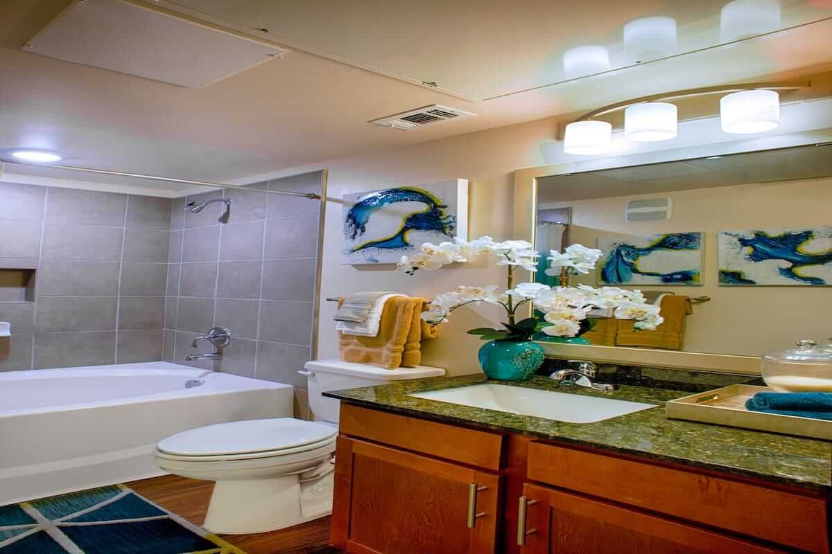 A modern bathroom featuring a sink with a mirror, toilet, bathtub, and decorative elements including flowers and wall art.