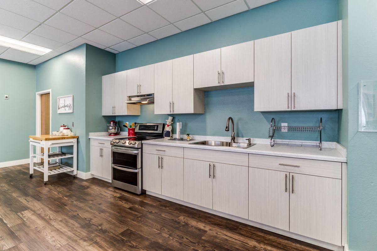 A modern kitchen with white cabinets, stainless steel appliances, and hardwood floors against a blue painted wall.