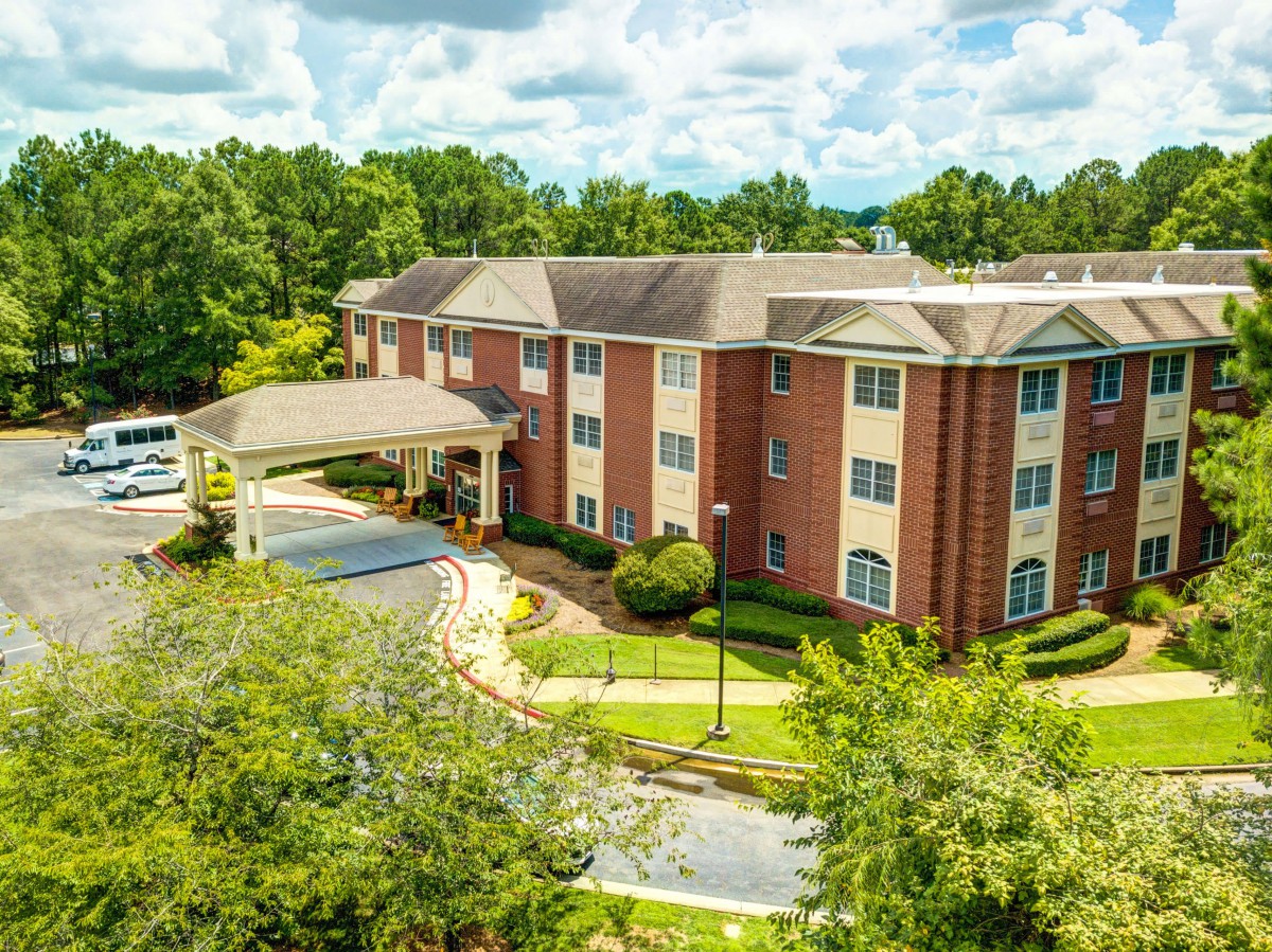Aerial view of a residential brick building surrounded by lush greenery and a curved driveway.