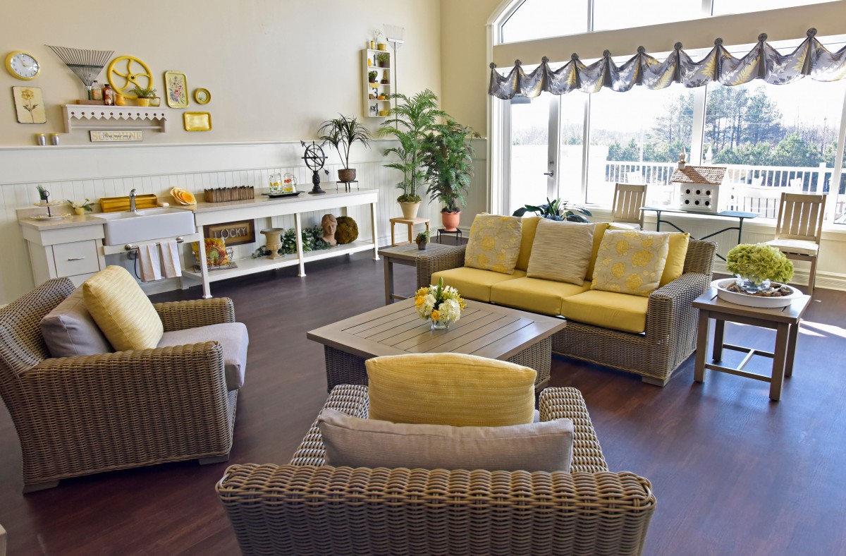 A cozy living room with wicker furniture and yellow accents, featuring a large window and decorative elements.