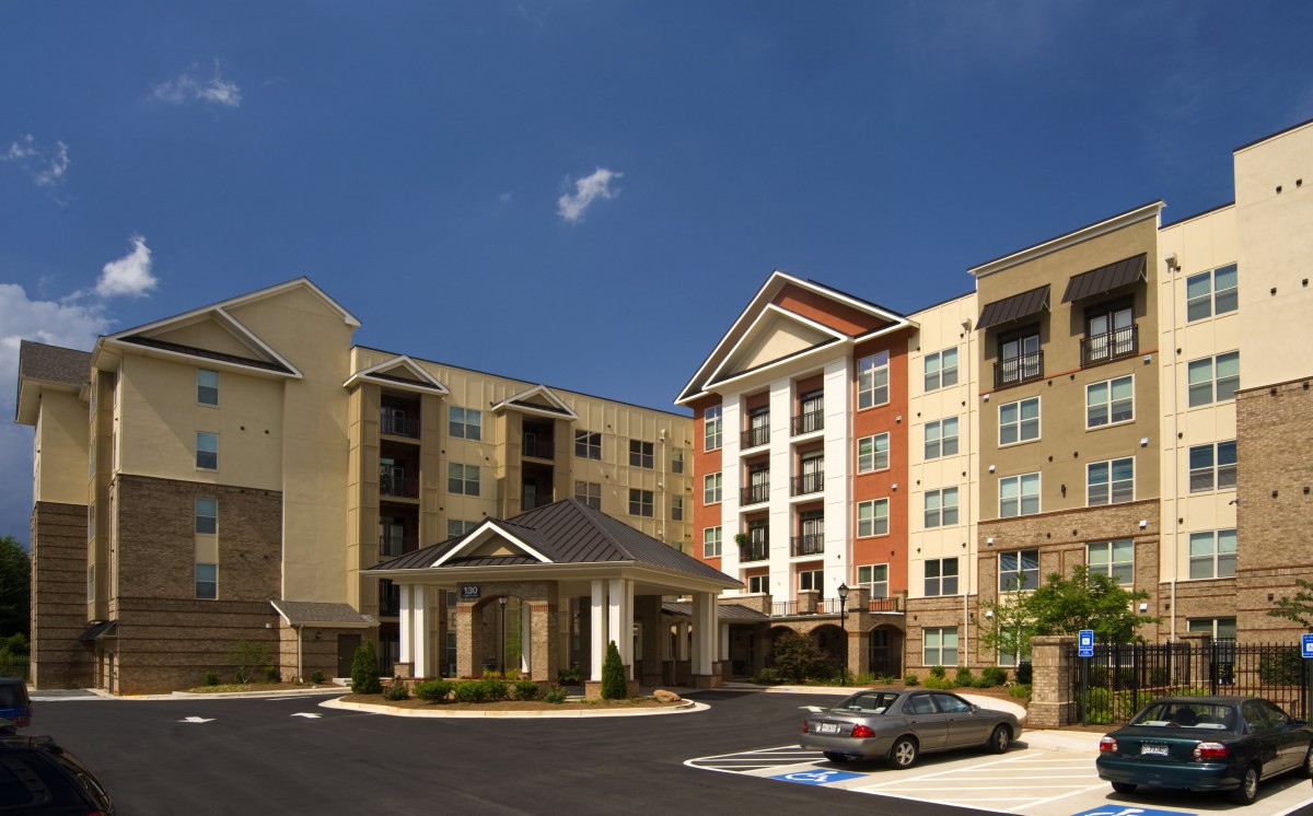 A modern apartment building with a parking lot under a clear blue sky.
