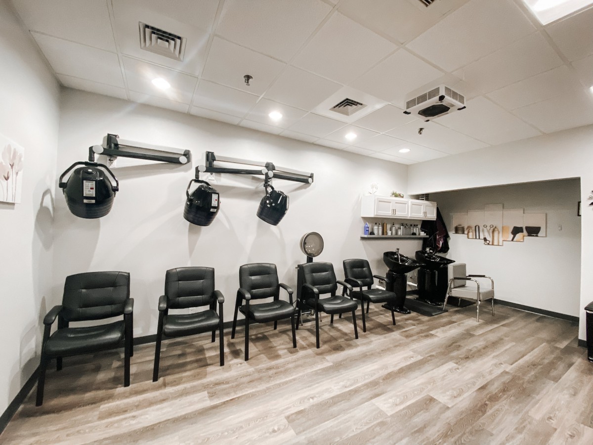 A modern salon interior with a row of chairs and wall-mounted hair dryers.