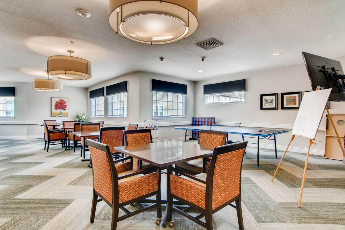 A spacious game room featuring a ping pong table, tables with orange chairs, and stylish lighting.