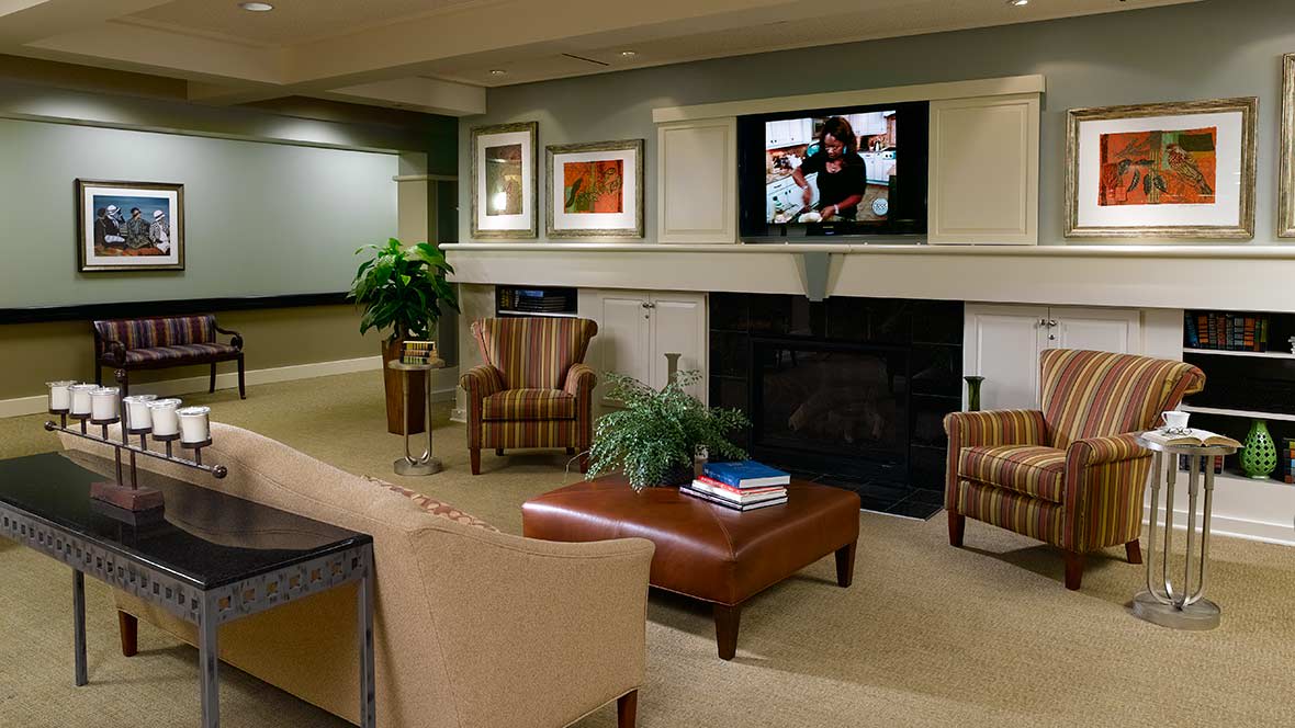 A cozy living room with a sofa, armchairs, and a coffee table facing a fireplace topped with a television.