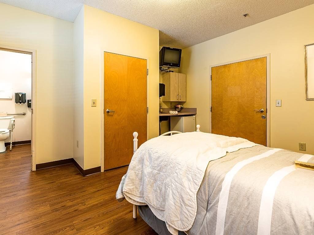 A minimalist bedroom with a bed, doors, and compact storage area.