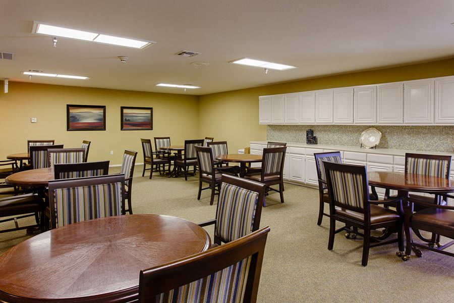 An empty dining room with multiple tables and chairs, adjacent to a kitchenette area.