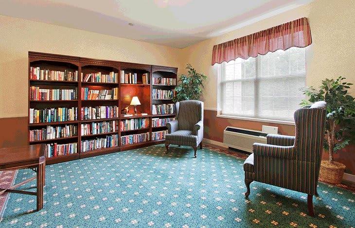 A cozy reading room with a bookshelf, armchair, and a large window.