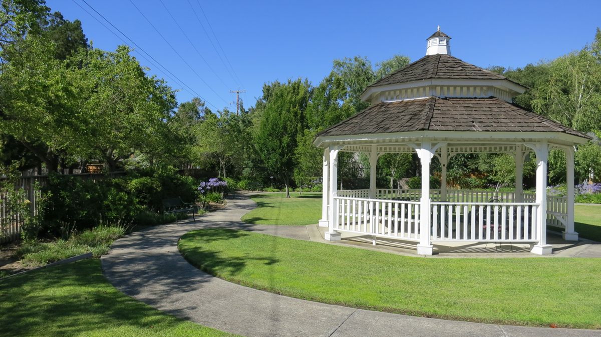 A peaceful park scene featuring a gazebo surrounded by lush greenery and a winding walkway.