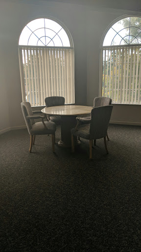 A cozy meeting room with a round table and four chairs, illuminated by natural light from the blinds.