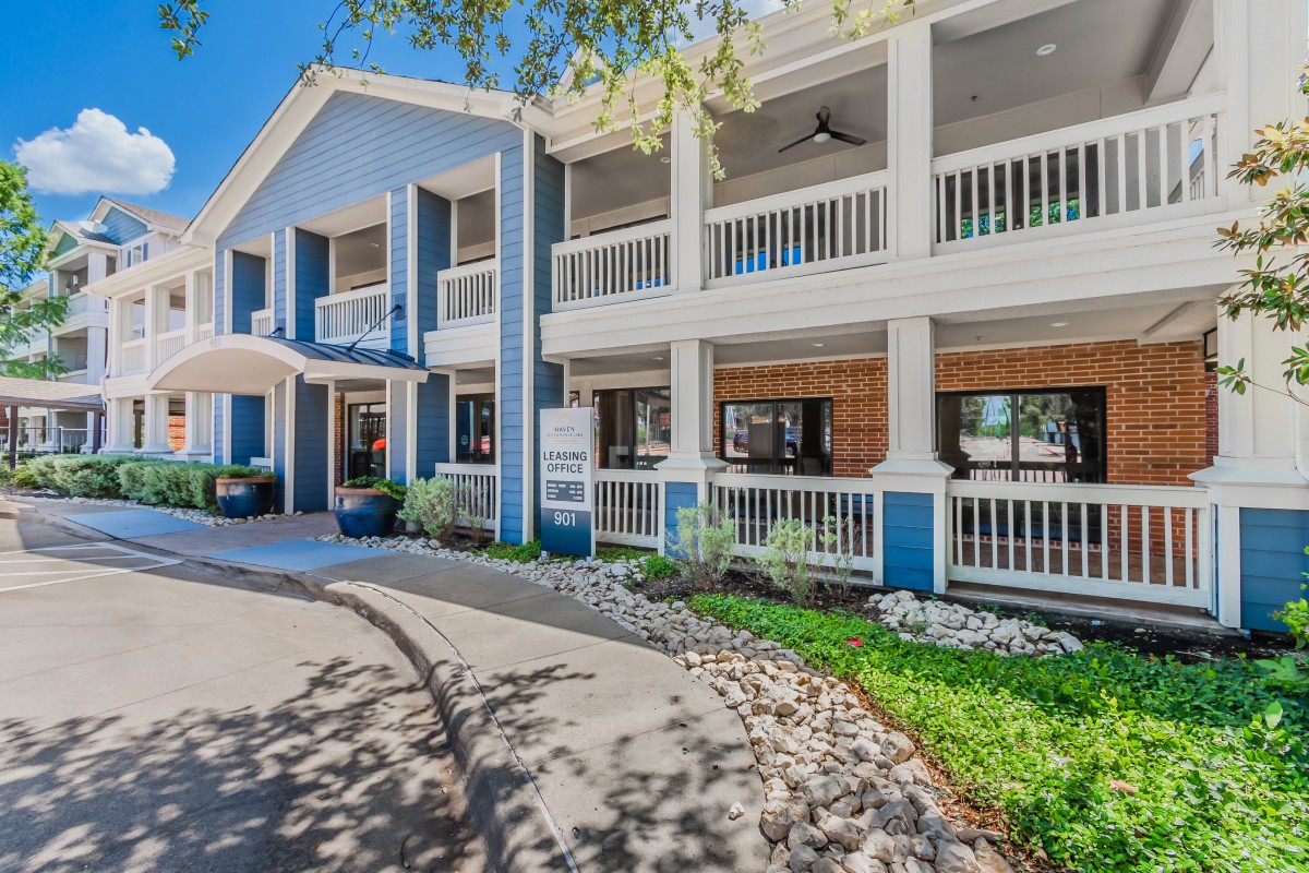 A two-story building with blue and white exterior featuring balconies and landscaped surroundings.