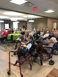 A group of elderly people in wheelchairs gathered in a nursing home common area.