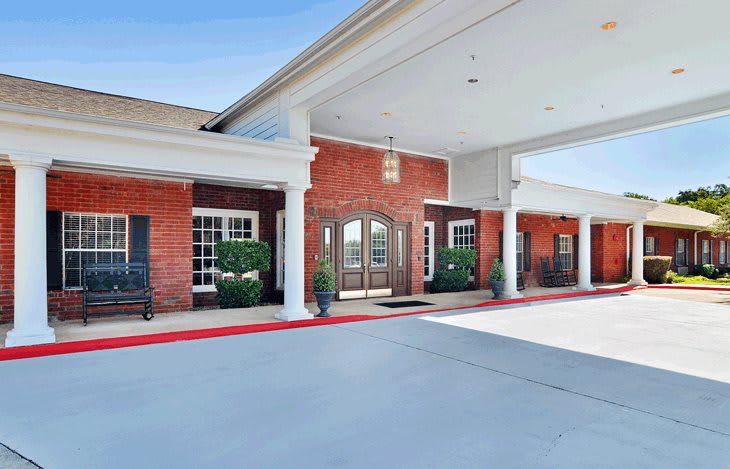 Entrance of a red brick building with a covered walkway and white columns.