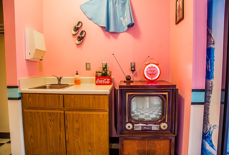 A vintage kitchen setup featuring a retro television against pink walls, capturing the essence of a 1950s style.