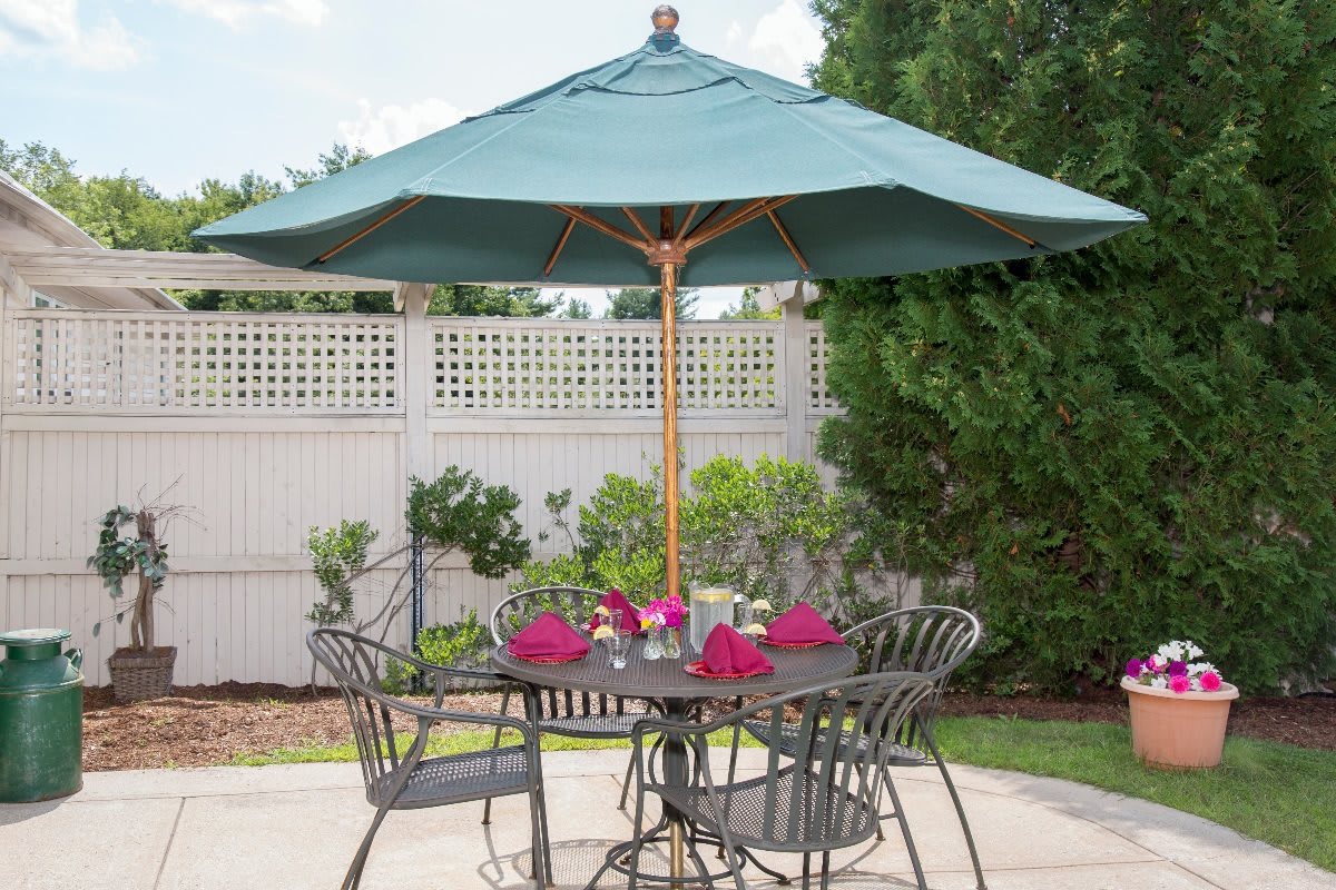A patio set with a table and chairs under a large umbrella in a garden setting.