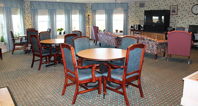 A cozy living room with a round wooden table and chairs, featuring patterned curtains and carpet.