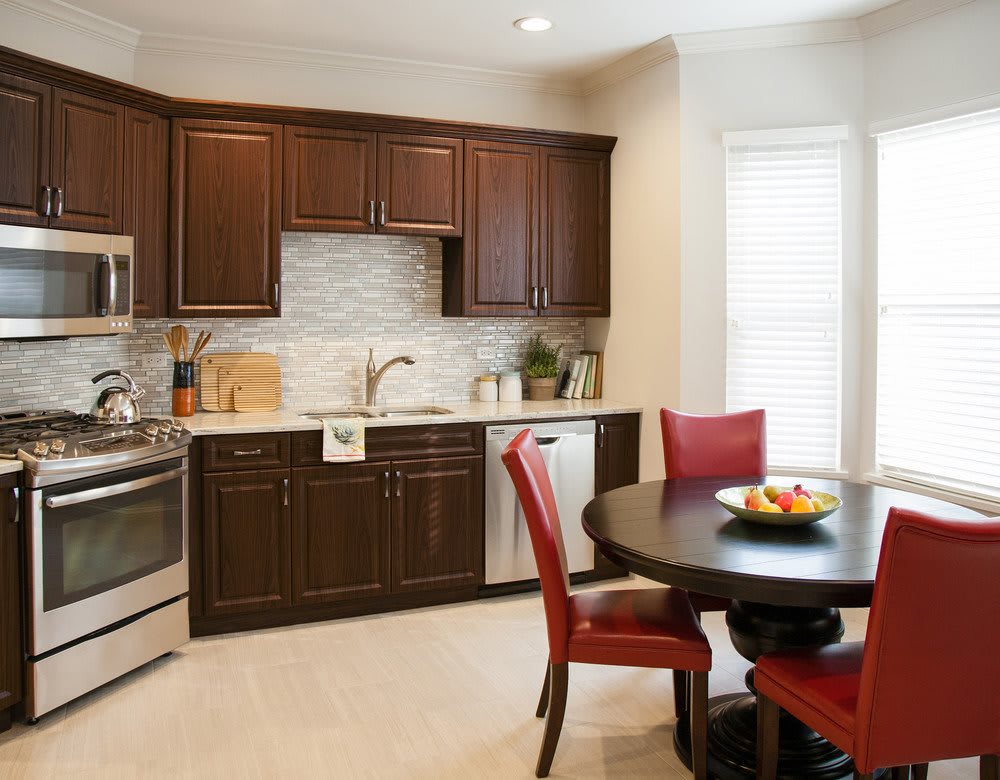 A modern kitchen featuring dark cabinetry, a round dining table with red chairs, and a stylish backsplash.