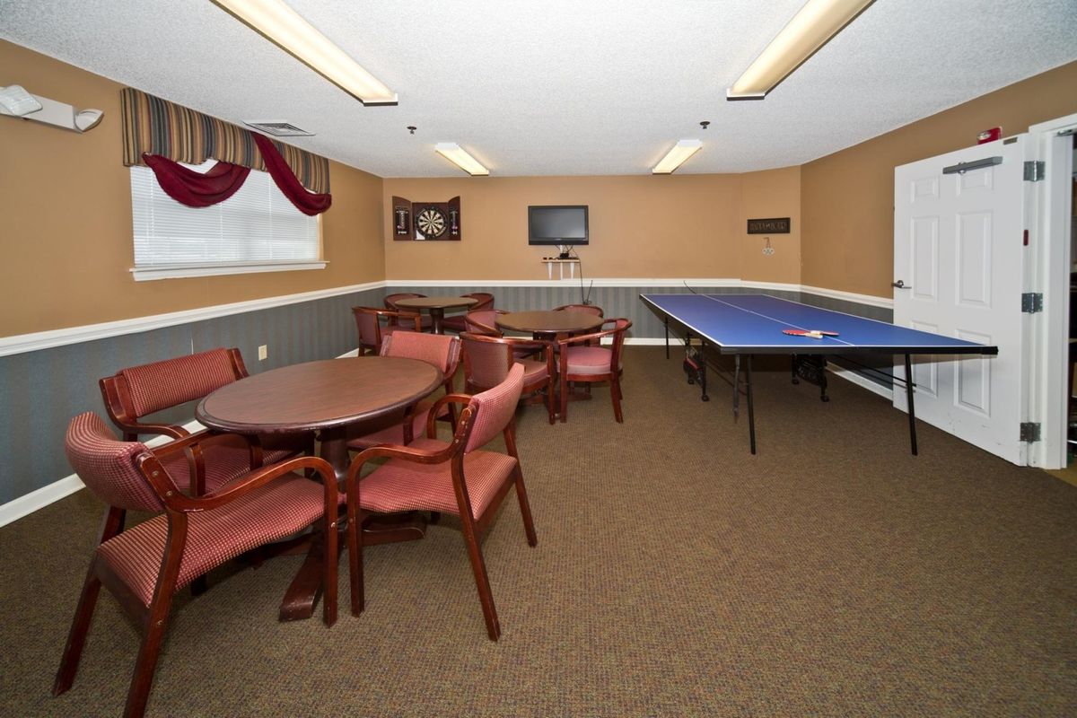 A recreational room featuring a table for table tennis, wooden tables and chairs, a television mounted on the wall, and carpeted flooring.