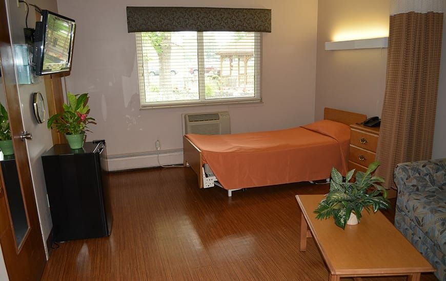 A tidy, simple bedroom featuring a single bed with an orange cover, wooden flooring, and decorative indoor plants.