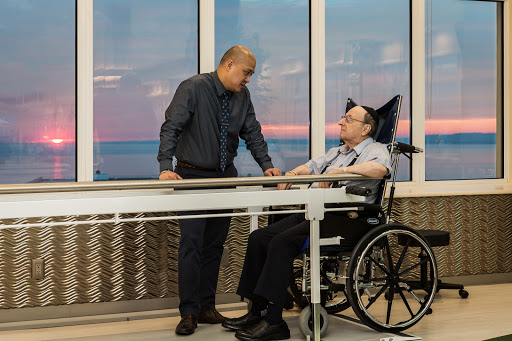 A caregiver engages with a patient in a wheelchair as the sun sets outside, highlighting a moment of support and connection.