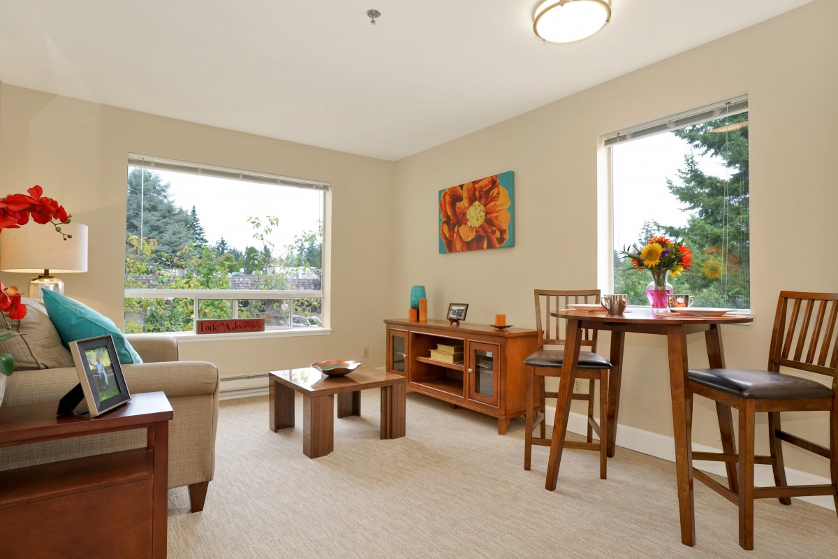 A cozy living room filled with natural light, featuring modern wooden furniture and vibrant artwork on the wall.