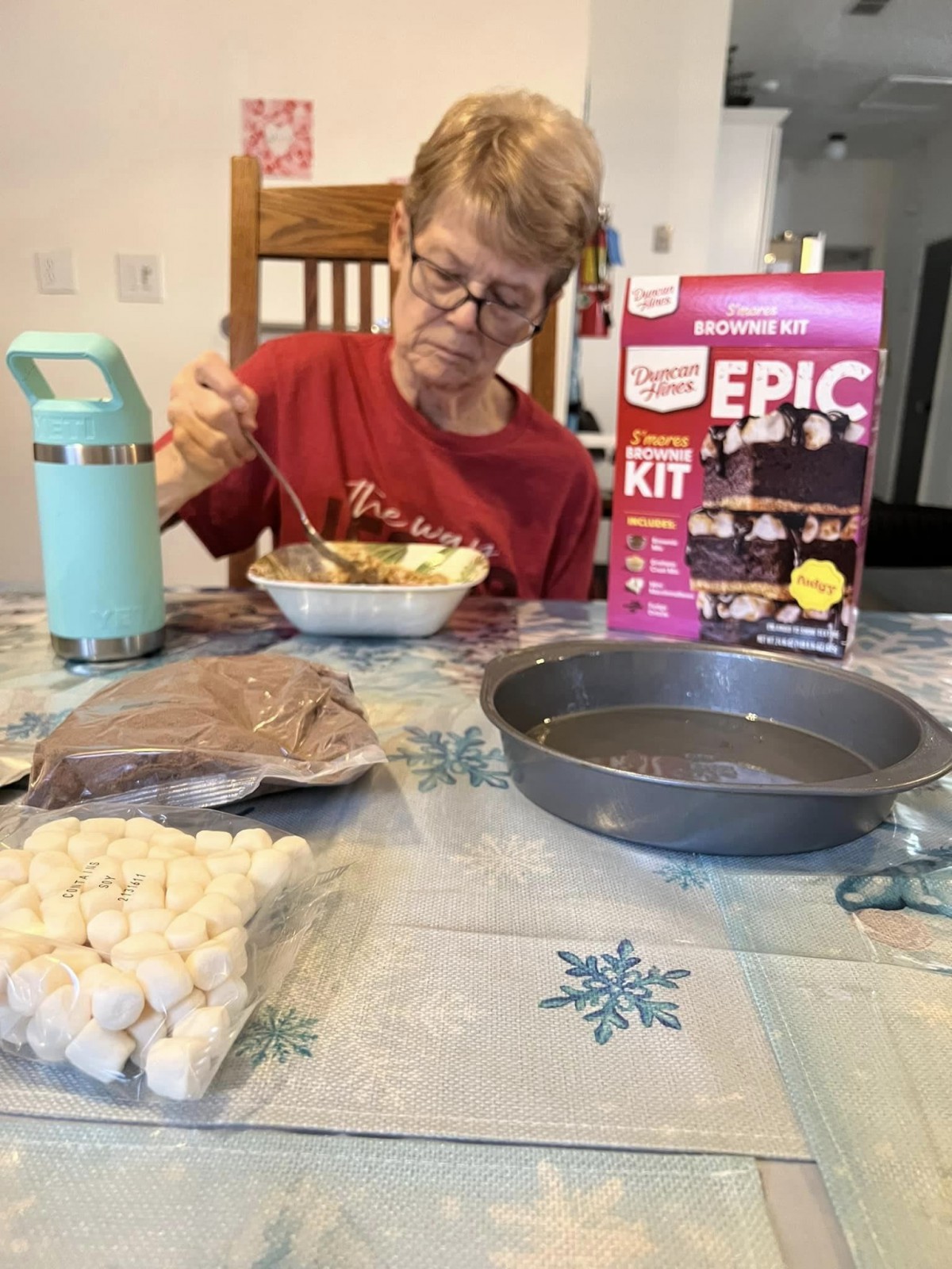 A person preparing a cake using an Epic baking kit at a kitchen table.