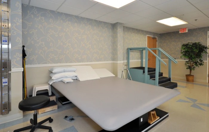 A physical therapy room equipped with a padded exercise table and rehabilitation stairs.