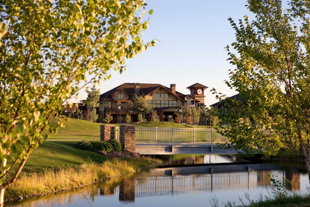 A scenic view of a golf course with a clubhouse, bridge, and pond at sunset.