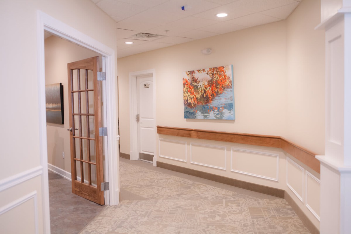 A well-lit hallway with a wooden door, adorned with a colorful painting on the wall.
