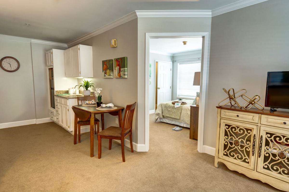 A cozy living space with a small dining area and an adjacent kitchen, featuring classic furniture and warm decor.