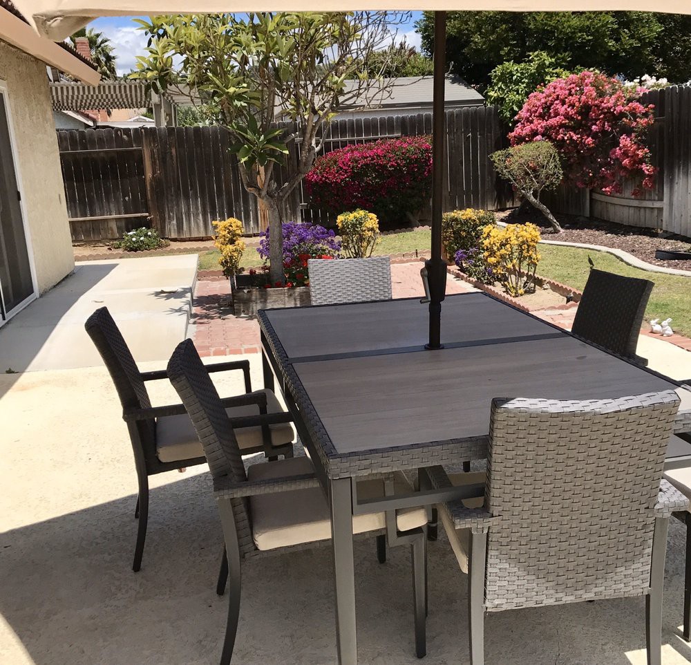 A backyard patio with a table, chairs, and an umbrella, surrounded by a garden.