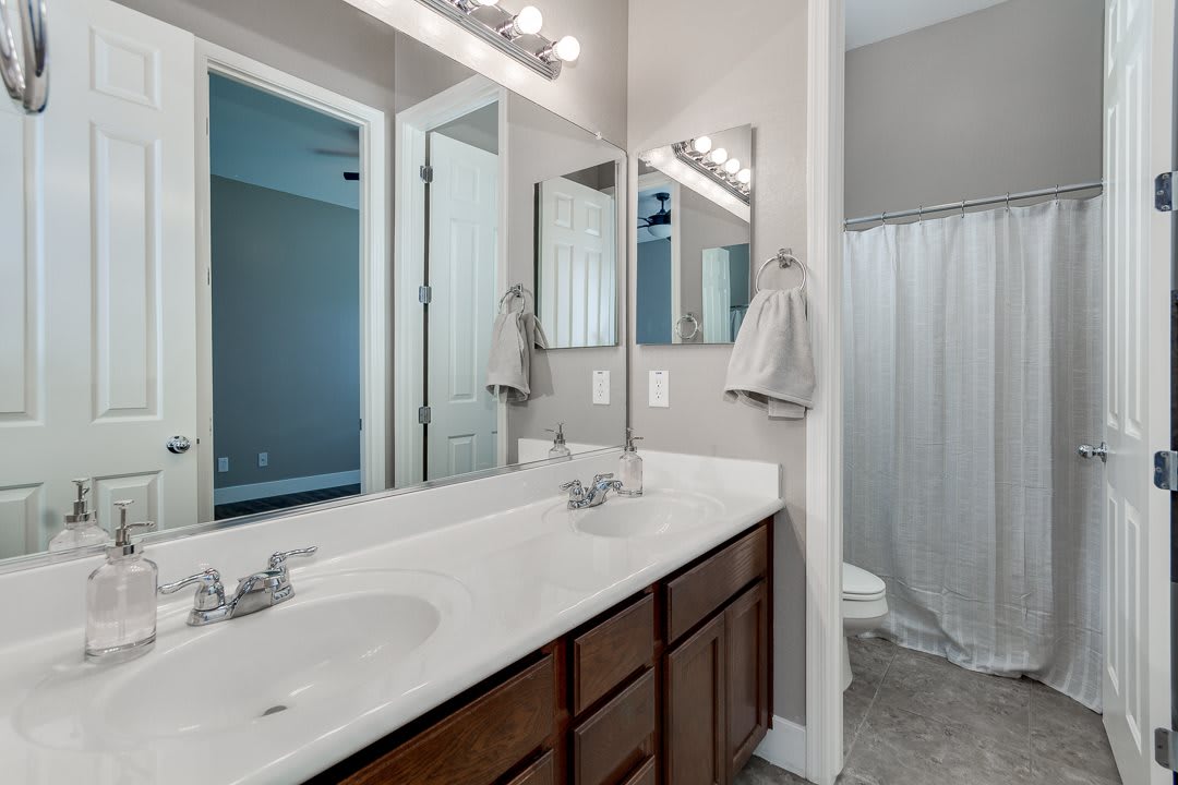 A modern bathroom featuring a double sink with large mirrors and a shower area with a curtain.