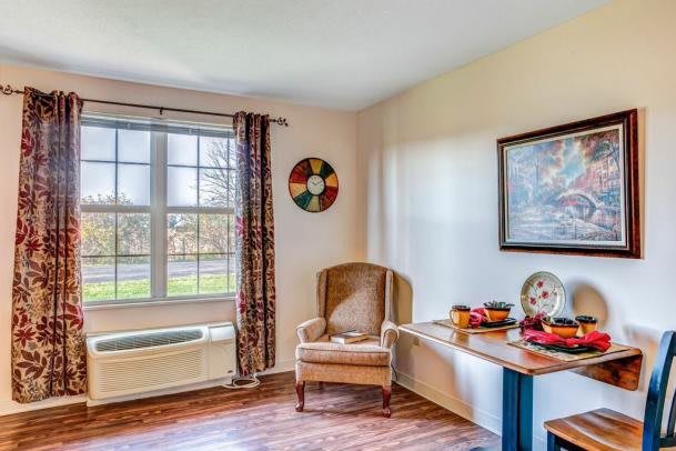 A cozy living room corner with an armchair near a window, accompanied by wall art and a decorated table.