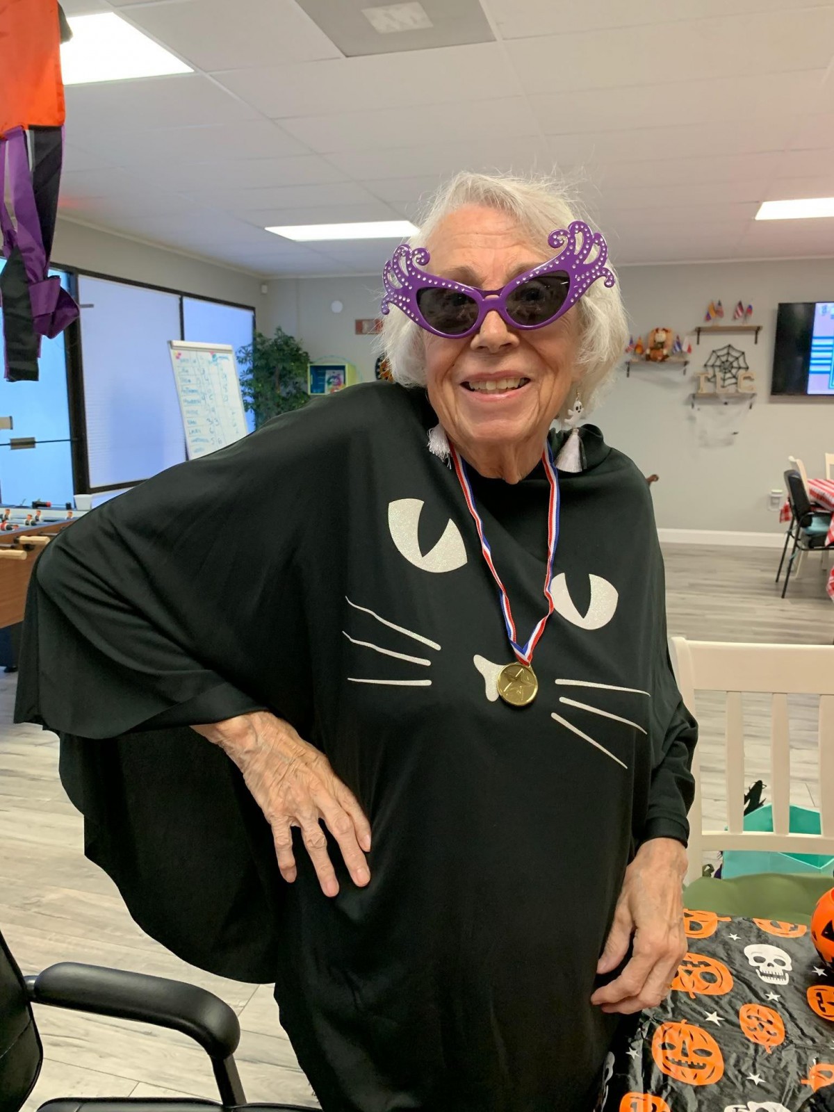 An elderly woman wearing a cat-themed costume and sunglasses, smiling indoors.