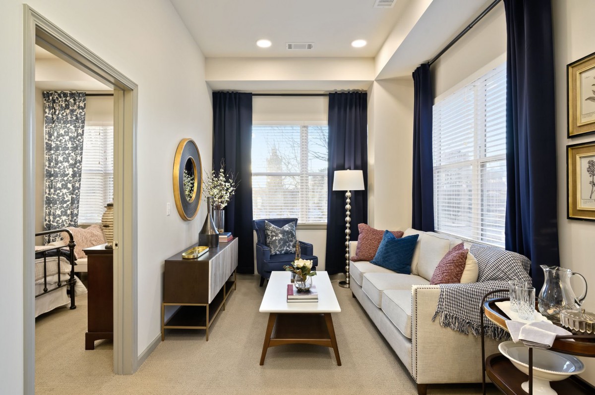 A modern living room with neutral tones, featuring a comfortable sofa, stylish coffee table, and floor lamp. The space is enhanced by blue curtains and ample natural light.