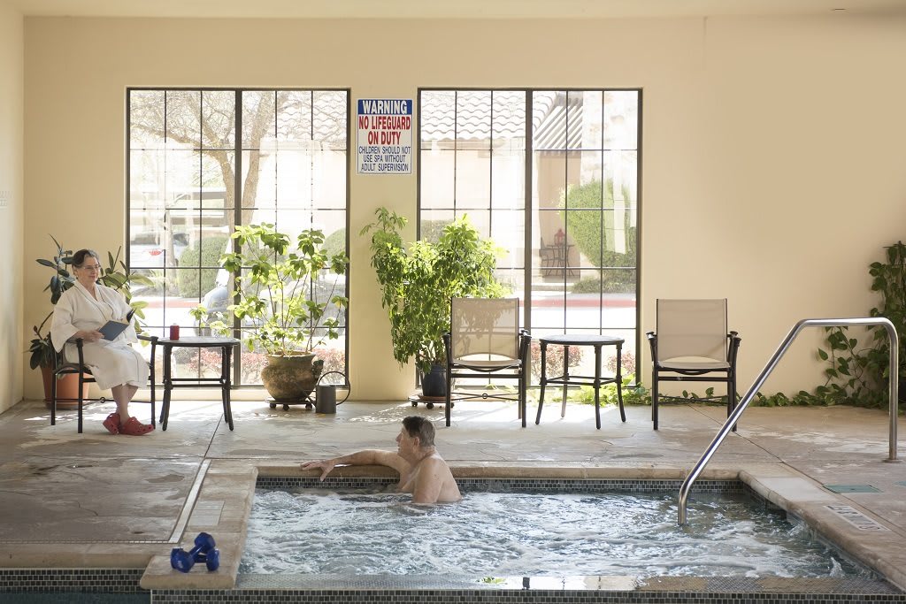 A person relaxing in an indoor jacuzzi with chairs and plants in the background.