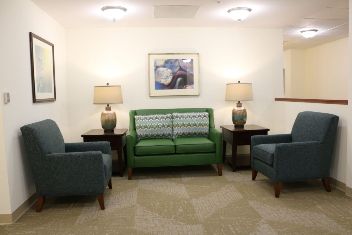 A cozy waiting room with a green sofa, two armchairs, and two lamps on side tables.