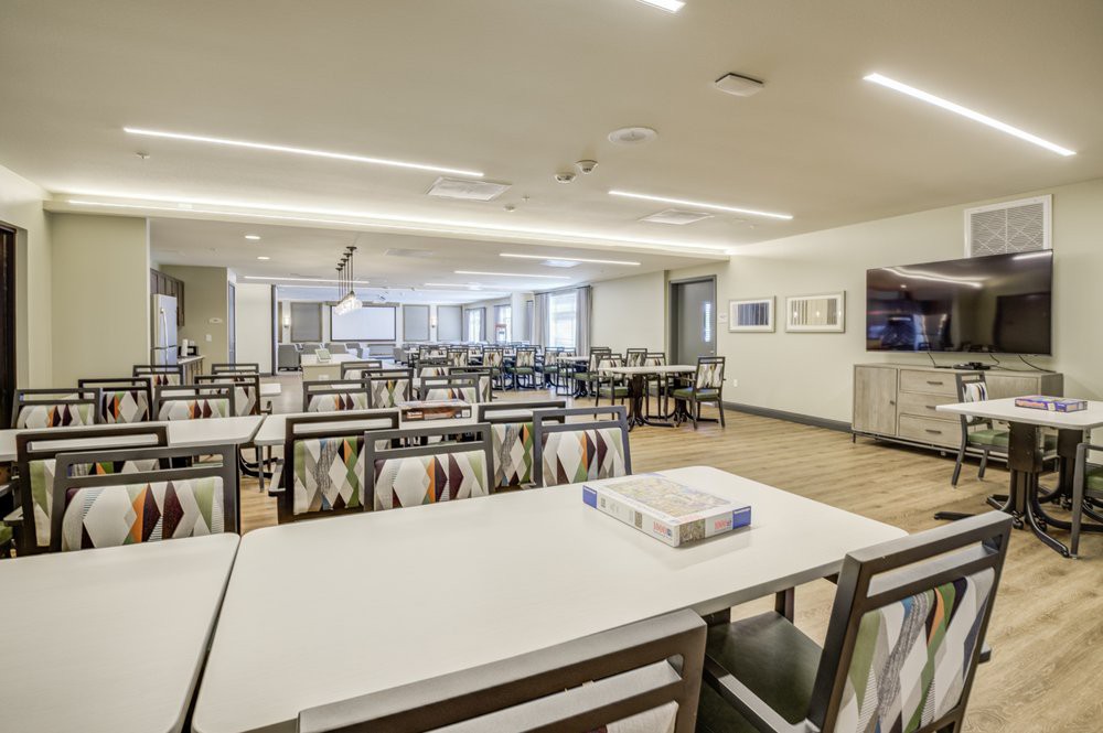 A spacious, modern dining hall with neatly arranged tables and chairs, illuminated by overhead lighting.