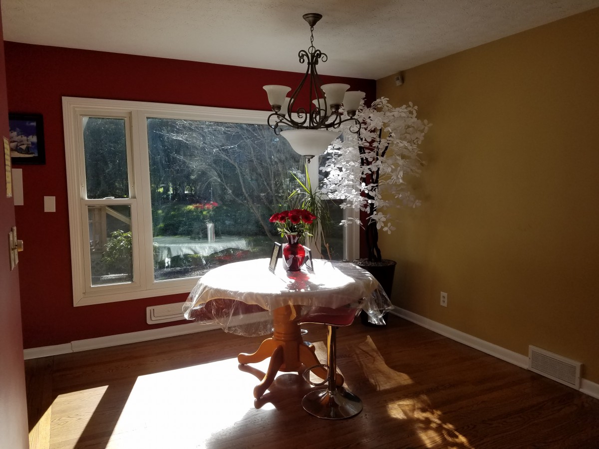 A sunlit dining room with a table and chairs under a chandelier, featuring a decorative bouquet of flowers.