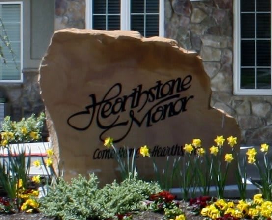 A decorative stone sign with 'Hearthstone Manor' inscribed, surrounded by blooming flowers.