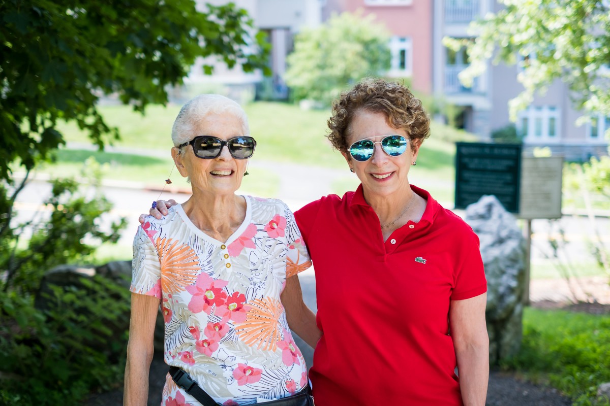 Two women smiling and wearing sunglasses while enjoying a sunny day outdoors.